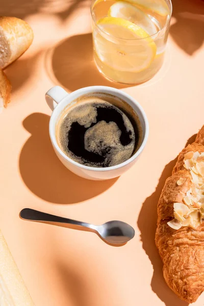 Café, água e croissant para o café da manhã na mesa bege — Fotografia de Stock
