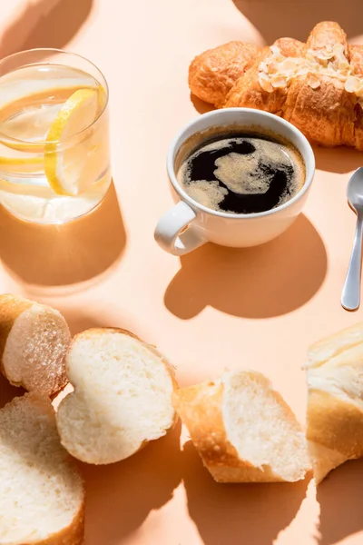 Tasse de café, croissant, eau et baguette pour le petit déjeuner sur table beige — Photo de stock