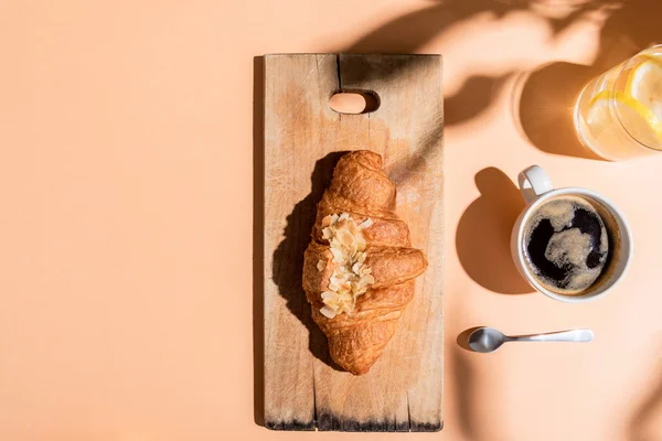 Top view of coffee, water and croissant on wooden board for breakfast on beige table — Stock Photo