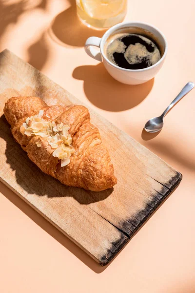 Croissants frescos na placa de madeira e xícara de café para o café da manhã na mesa bege — Fotografia de Stock