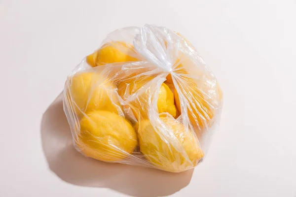 Свежие желтые лимоны в пластиковом пакете на сером столе — стоковое фото