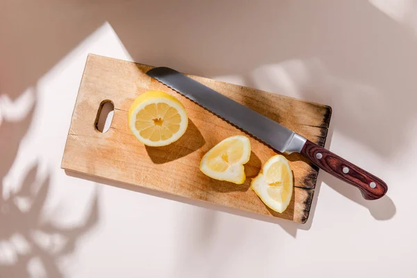 Top view of cutted lemon on wooden board with knife on grey table with shadows — Stock Photo