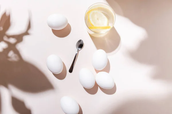 Top view of boiled eggs, glass of water with lemon and teaspoon on grey table with shadows — Stock Photo
