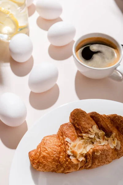 Eggs, croissant, coffee and water with lemon for breakfast on grey table with shadows — Stock Photo