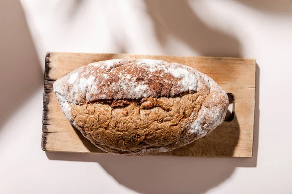 Top view of bread on cutting board on grey table with shadows — Stock Photo