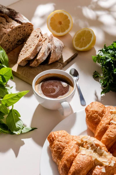 Fresh croissants, bread, greenery and cup of coffee for breakfast on grey table — Stock Photo