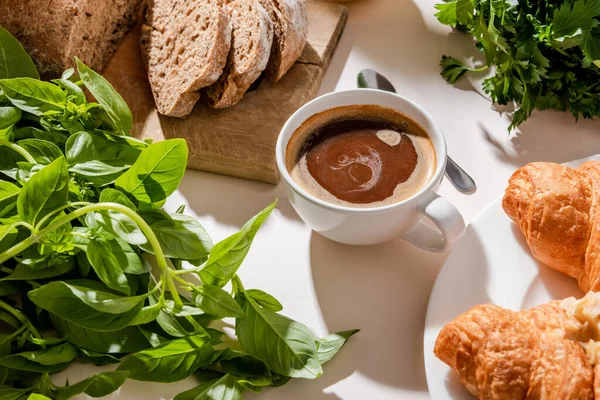 Pan, croissants, vegetación y taza de café para el desayuno en la mesa gris - foto de stock