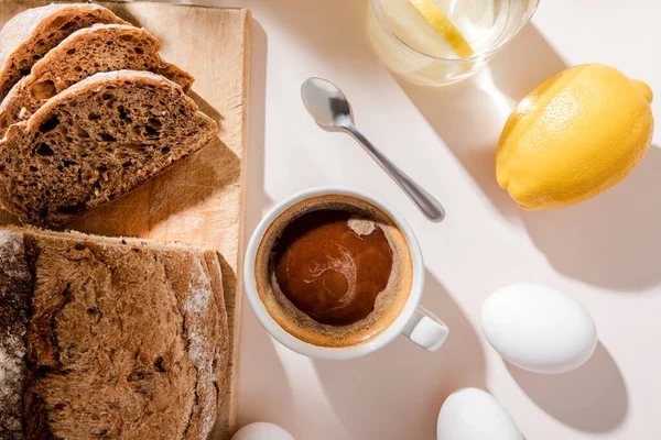 Vue de dessus du pain, des oeufs, de l'eau de citron et de la tasse de café pour le petit déjeuner sur la table grise — Photo de stock
