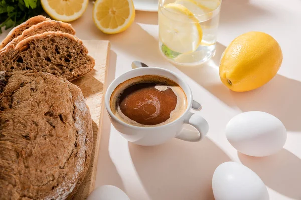 Pão, ovos, água de limão e xícara de café para o café da manhã na mesa cinza — Fotografia de Stock