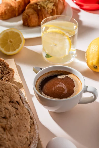 Primer plano de pan, agua de limón y taza de café para el desayuno en la mesa gris - foto de stock