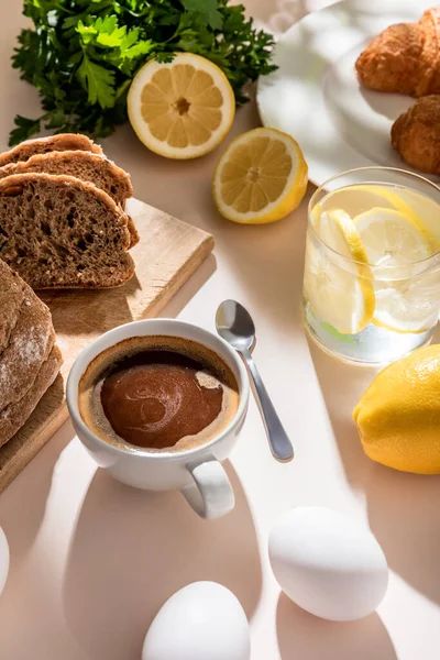 Pan fresco, huevos, agua de limón y taza de café para el desayuno en la mesa gris - foto de stock