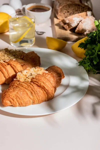 Cruasanes frescos, pan, café y agua de limón para el desayuno en la mesa gris, enfoque selectivo - foto de stock