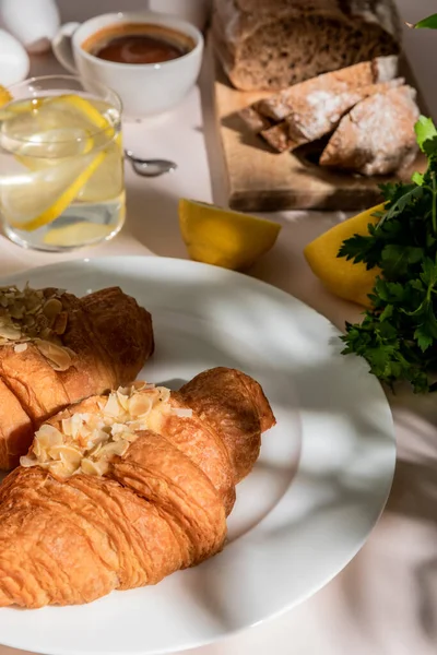 Cruasanes frescos, pan, café y agua de limón para el desayuno en la mesa gris, enfoque selectivo - foto de stock