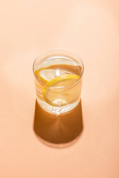 Glass of fresh water with lemon slices on beige with shadow — Stock Photo