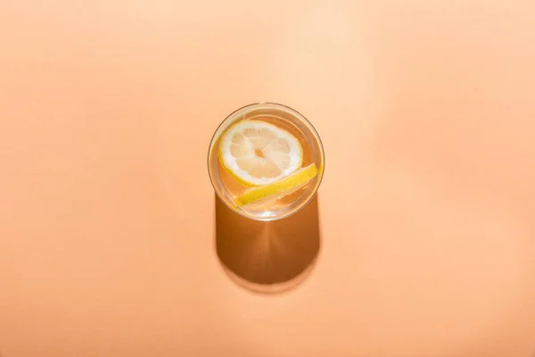 Top view of fresh water with lemon slices in glass on beige with shadow — Stock Photo