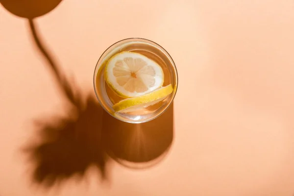 Вид сверху на пресную воду с ломтиками лимона в стекле на бежевом фоне с тенями — стоковое фото