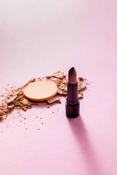 Cracked face powder near makeup sponge and lipstick on pink — Stock Photo