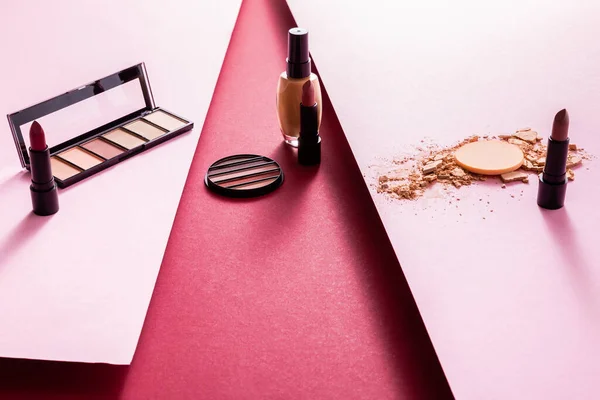 Eye shadow, lipsticks and face foundation near crushed face powder on pink and crimson — Stock Photo