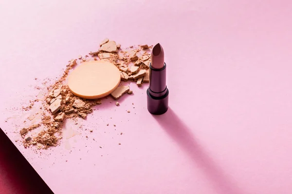Cracked face powder near lipstick and makeup sponge on pink — Stock Photo