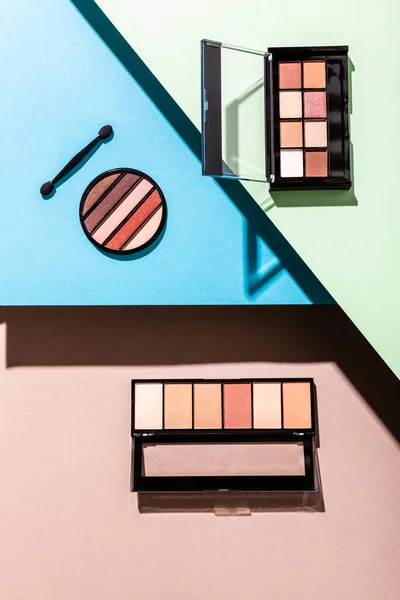 Top view of eye shadow palettes and double-sided eyeshadow applicator on pink, blue and green — Stock Photo