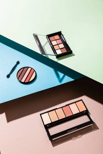 Eye shadow palettes and double-sided eyeshadow applicator on blue, green and pink — Stock Photo