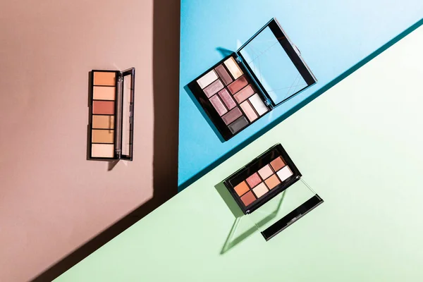 Top view of eye shadow palettes on blue, green and pink — Stock Photo