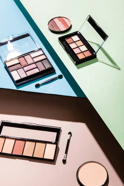 Eye shadow palettes, face powder and double-sided eyeshadow applicators on blue, green and pink — Stock Photo