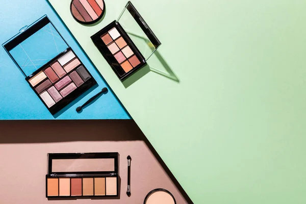 Top view of eye shadow palettes and double-sided eyeshadow applicators on blue, green and pink — Stock Photo