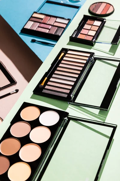Selective focus of eye shadow and blush palettes on green, blue and pink — Stock Photo