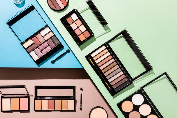 Top view of eye shadow and blush palettes near double-sided eyeshadow applicators on blue, green and pink — Stock Photo