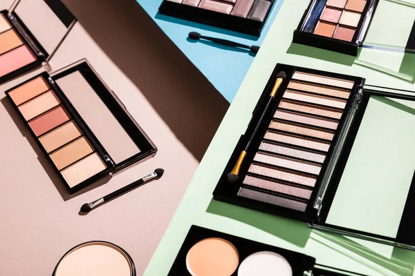 Fard à paupières et palettes blush près des pinceaux cosmétiques sur vert, bleu et rose — Photo de stock