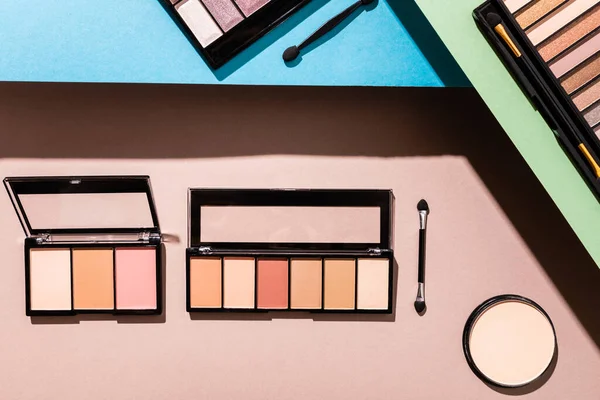 Top view of eye shadow palettes near double-sided eyeshadow applicators and face powder on blue, green and pink — Stock Photo