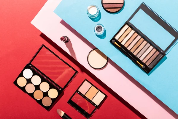 Top view of eye shadow palettes near cosmetic brushes, lipstick and face powder on crimson — Stock Photo