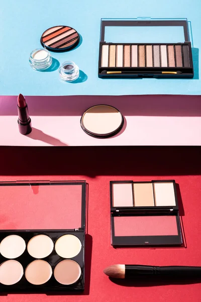 Palettes de fard à joues et de fard à paupières près des pinceaux cosmétiques, rouge à lèvres et poudre visage sur cramoisi, rose et bleu — Photo de stock