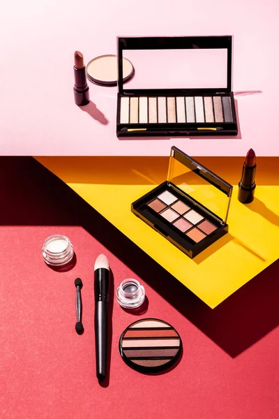 Eye shadow palettes and cosmetic brushes near lipsticks and face powder on crimson, pink and yellow — Stock Photo