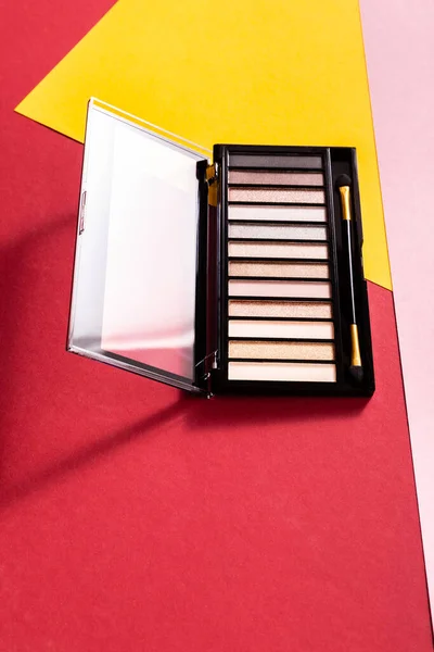 Eye shadow palette and double-sided eyeshadow applicator on crimson, pink and yellow — Stock Photo
