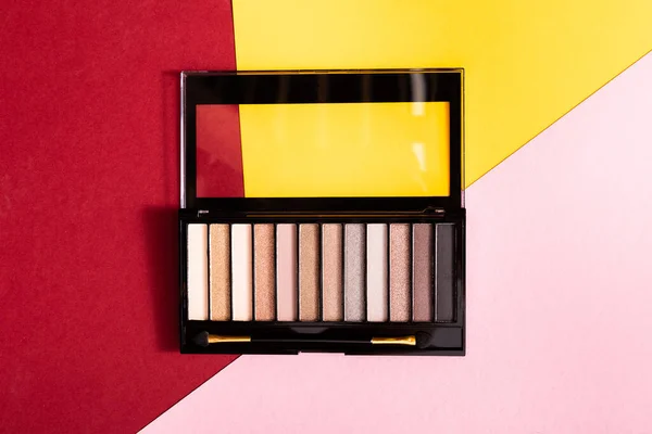 Top view of eye shadow palette and double-sided eyeshadow applicator on crimson, pink and yellow — Stock Photo