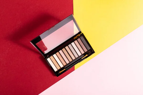 Top view of eye shadow palette and double-sided eyeshadow brush on crimson, pink and yellow — Stock Photo