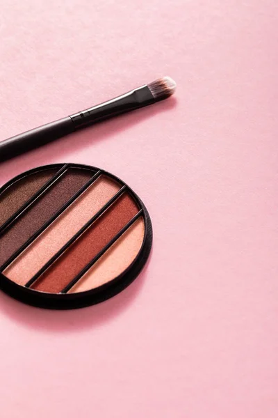 Paleta de colores y pastel sombra de ojos cerca de cepillo cosmético en rosa - foto de stock