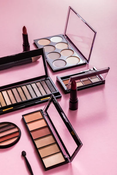 Eye shadow palettes and cosmetic brushes near lipsticks on pink — Stock Photo