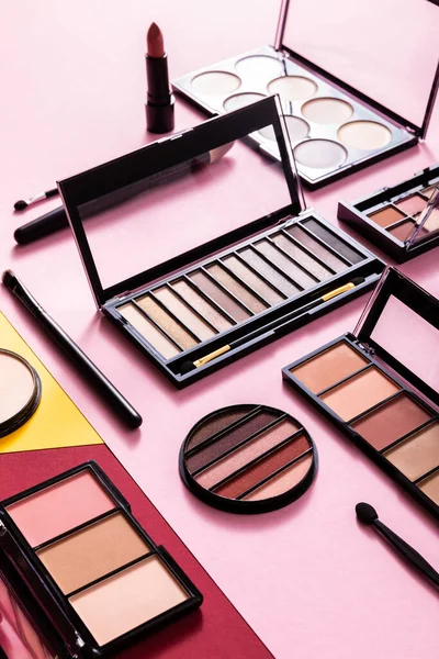 Eye shadow and blush palettes near cosmetic brushes and lipstick on pink — Stock Photo