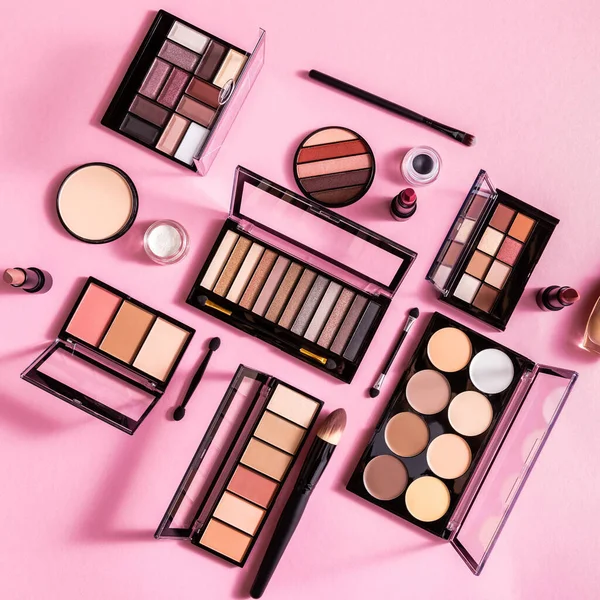 Top view of blush and eye shadow palettes near cosmetic brushes and lipsticks on pink — Stock Photo