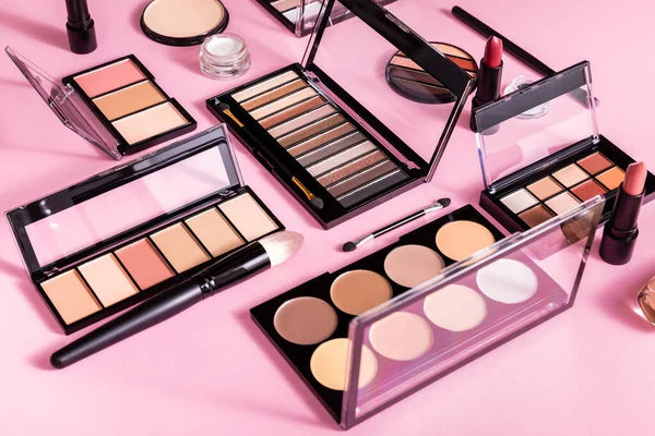 Paletas de colorete y sombra de ojos cerca de pinceles cosméticos y lápices labiales en rosa - foto de stock