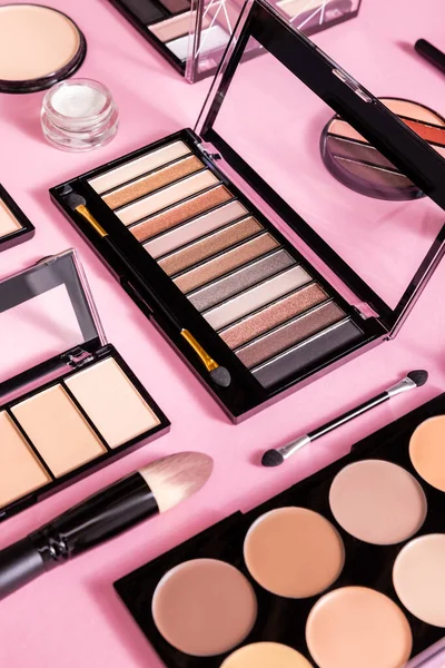 Eye shadow and blush palettes near cosmetic brushes and face powder on pink — Stock Photo