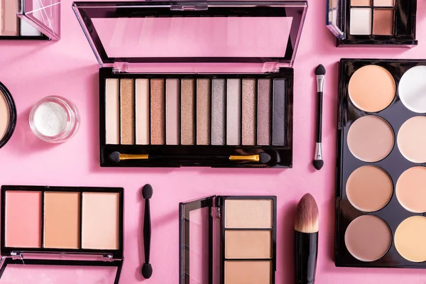 Top view of eye shadow and blush palettes near cosmetic brushes on pink — Stock Photo