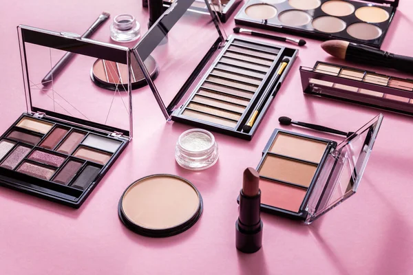 Eye shadow and blush palettes near face powder, cosmetic brushes and lipstick on pink — Stock Photo