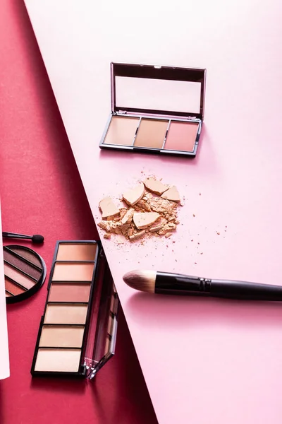 Eye shadow and blush palettes near cracked face powder and cosmetic brushes on pink and crimson — Stock Photo
