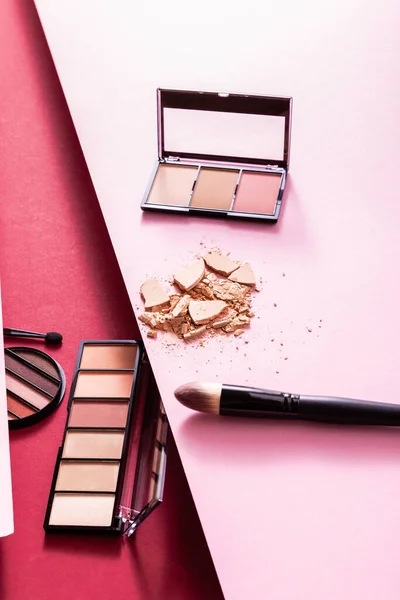 Fard à paupières et palettes blush près de la poudre pour le visage fissurée et pinceaux cosmétiques sur rose et cramoisi — Photo de stock