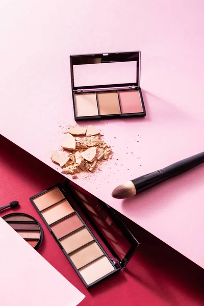 Eye shadow palettes near cracked face powder and cosmetic brushes on pink and crimson — Stock Photo