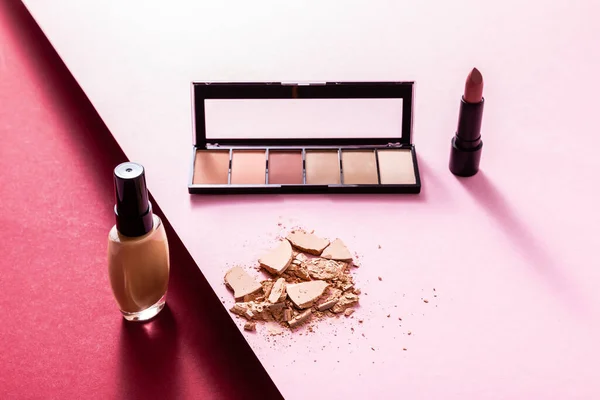 Gesichtsfundament nahe Lidschattenpalette, rissiges Gesichtspuder und Lippenstift auf rosa und purpurrot — Stockfoto